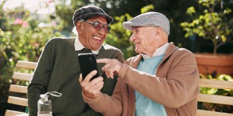 Lachende Herren sitzen auf der Bank, einer hält ein Smartphone